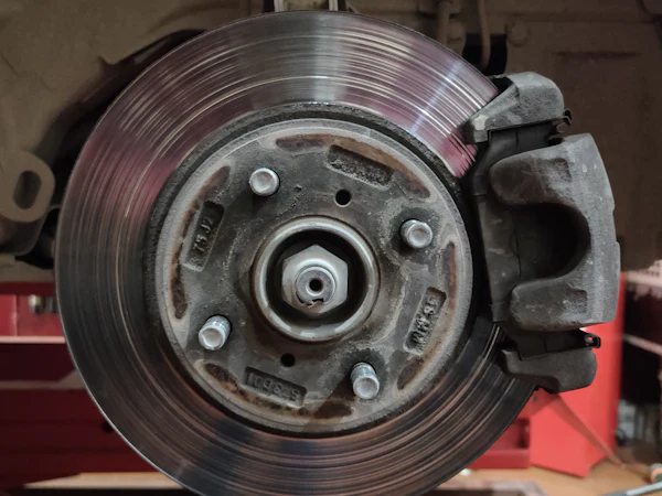 A worn brake disc and caliper on a hub with the wheel off