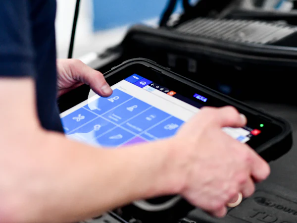 A hand working a diagnostic tablet plugged into a car