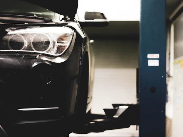 The front of a dark car raised on a two-post lift, in black and white