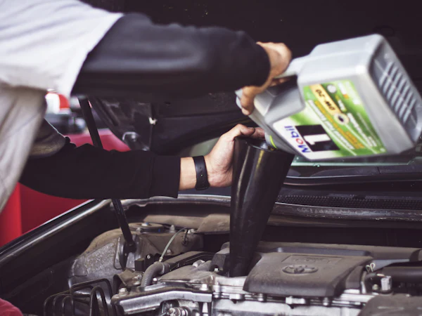 Gloved hands pouring fresh engine oil through a funnel into an open engine bay