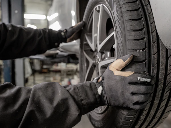 Gloved hands lifting a tyre onto a wheel hub in a workshop