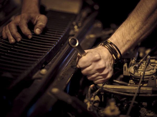 Hands with grease on them turning a spanner deep in an engine bay