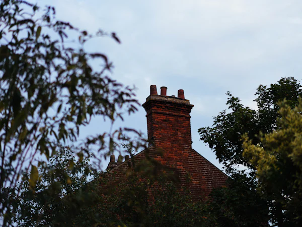 A red brick chimney stack above a tiled roof and trees