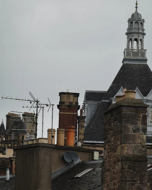 Stone chimneys and aerials against a grey sky, a turret behind