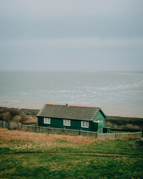 A green timber house on the coast with the grey sea beyond
