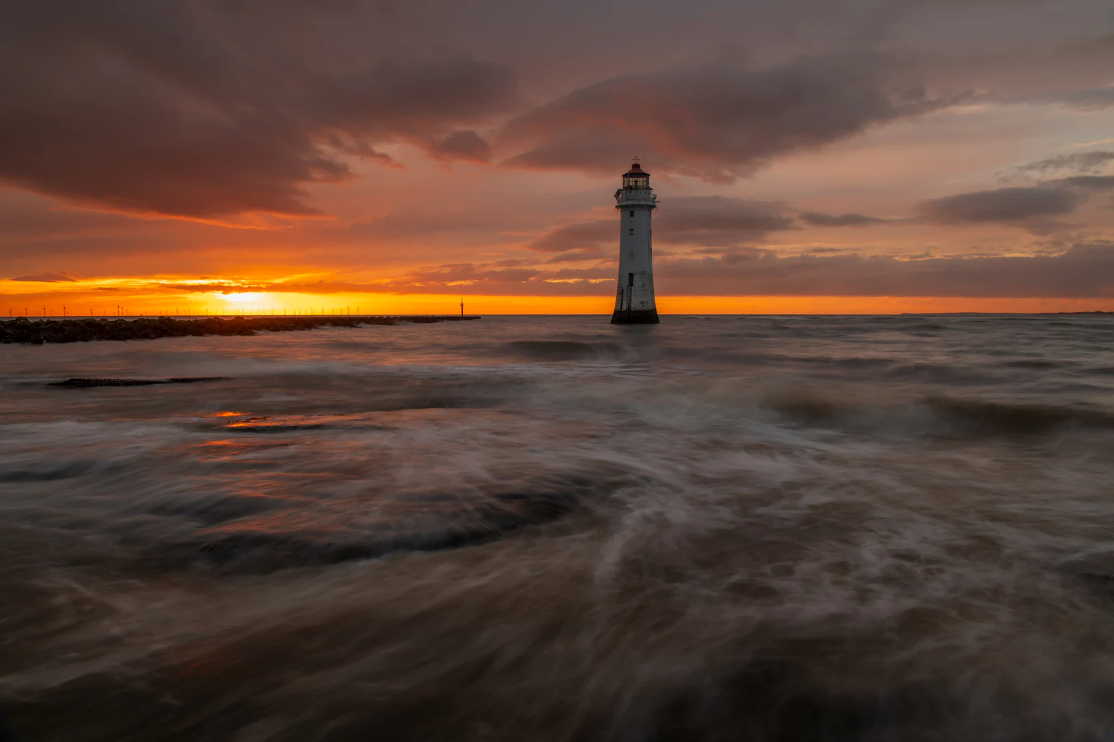 Perch Rock lighthouse at New Brighton at sunset, the tide streaming past it under a heavy sky