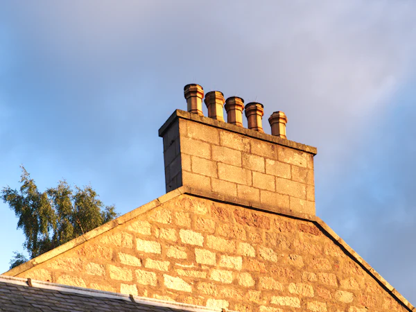 A sandstone chimney stack with five clay pots in low sun