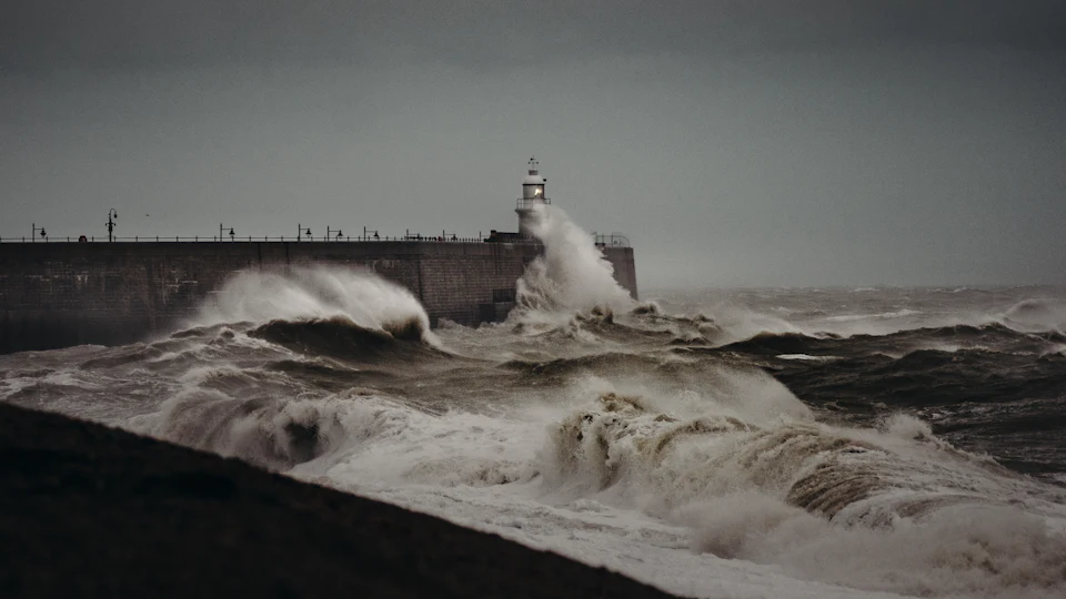 Storm waves breaking over a harbour wall and its lighthouse
