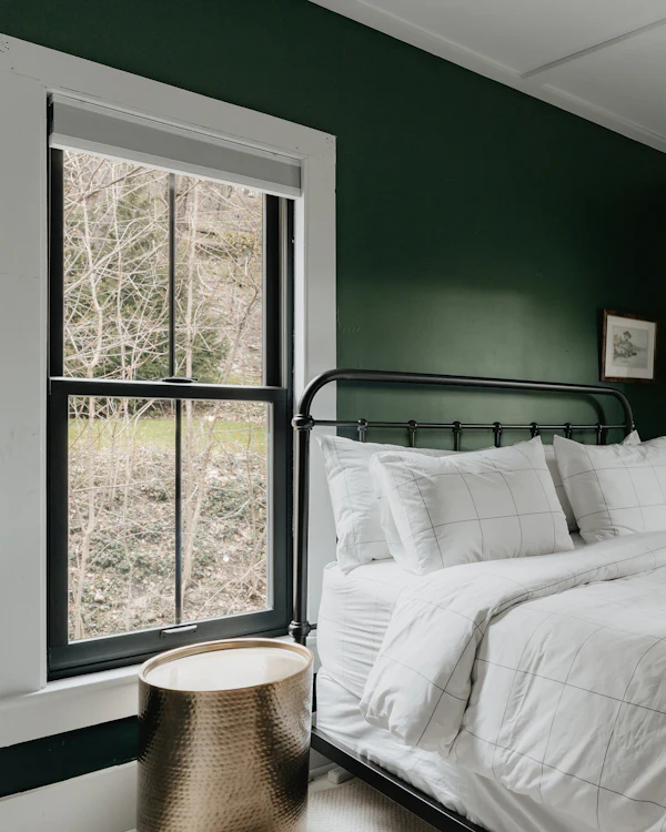 A bedroom in dark green with a white-framed sash window and an iron bed