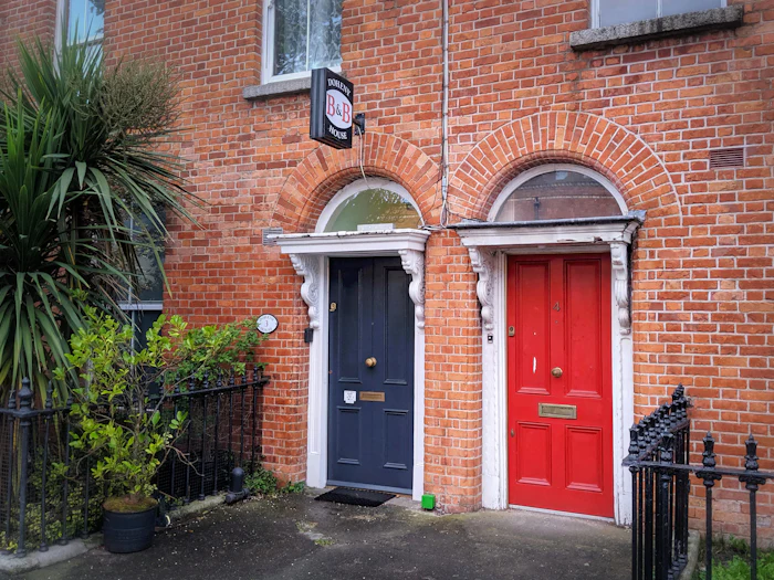 Two front doors side by side in a red brick terrace, one navy and one pillar-box red, under white fanlights