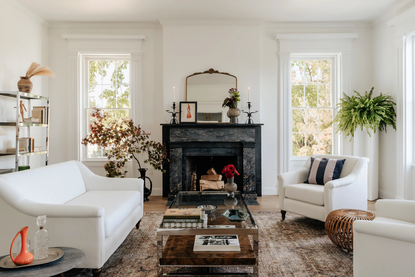 A tall front room with two sash windows in deep white architraves either side of a chimney breast, a black marble fireplace, a gilt mirror, white sofas and a fern