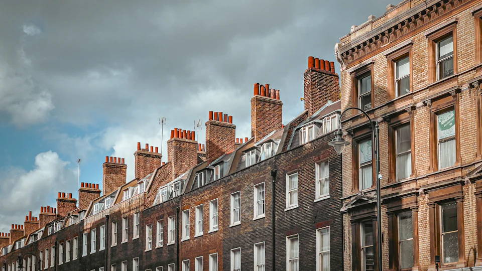 A long Victorian red brick terrace with tall chimneys under a cloudy sky