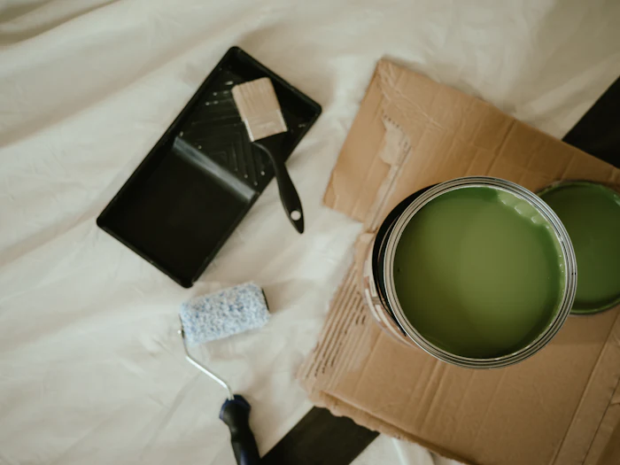 An open tin of green paint, a roller and a tray on a dust sheet