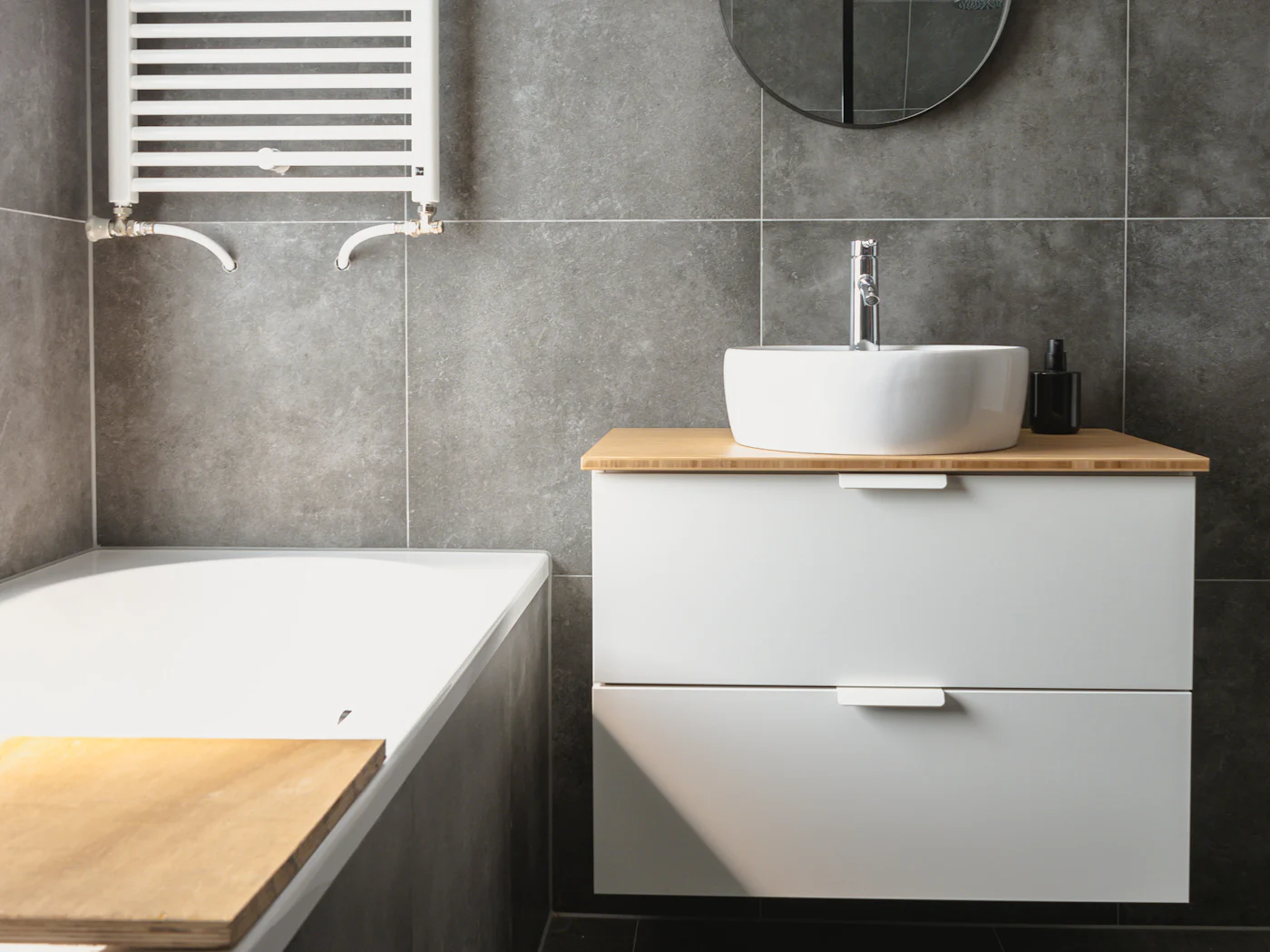 The finished bathroom: grey tiles, a bath, a vanity basin and a chrome towel rail