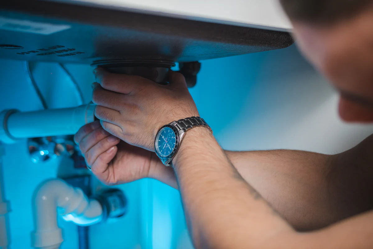 Hands tightening a fitting on the pipes under a sink