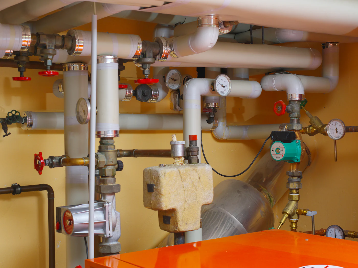 A new heating system: insulated pipes, valves, gauges and a pump on a yellow wall