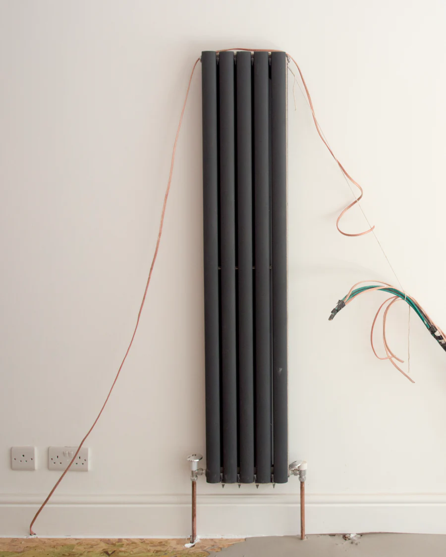 A slim vertical radiator on a white wall, its pipes coming up through the floor