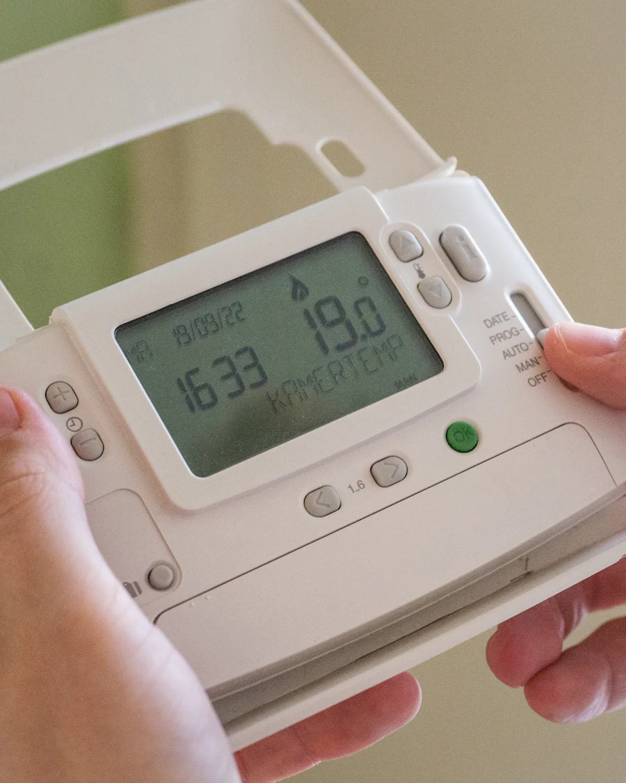 Hands holding a programmable heating thermostat showing 19 degrees