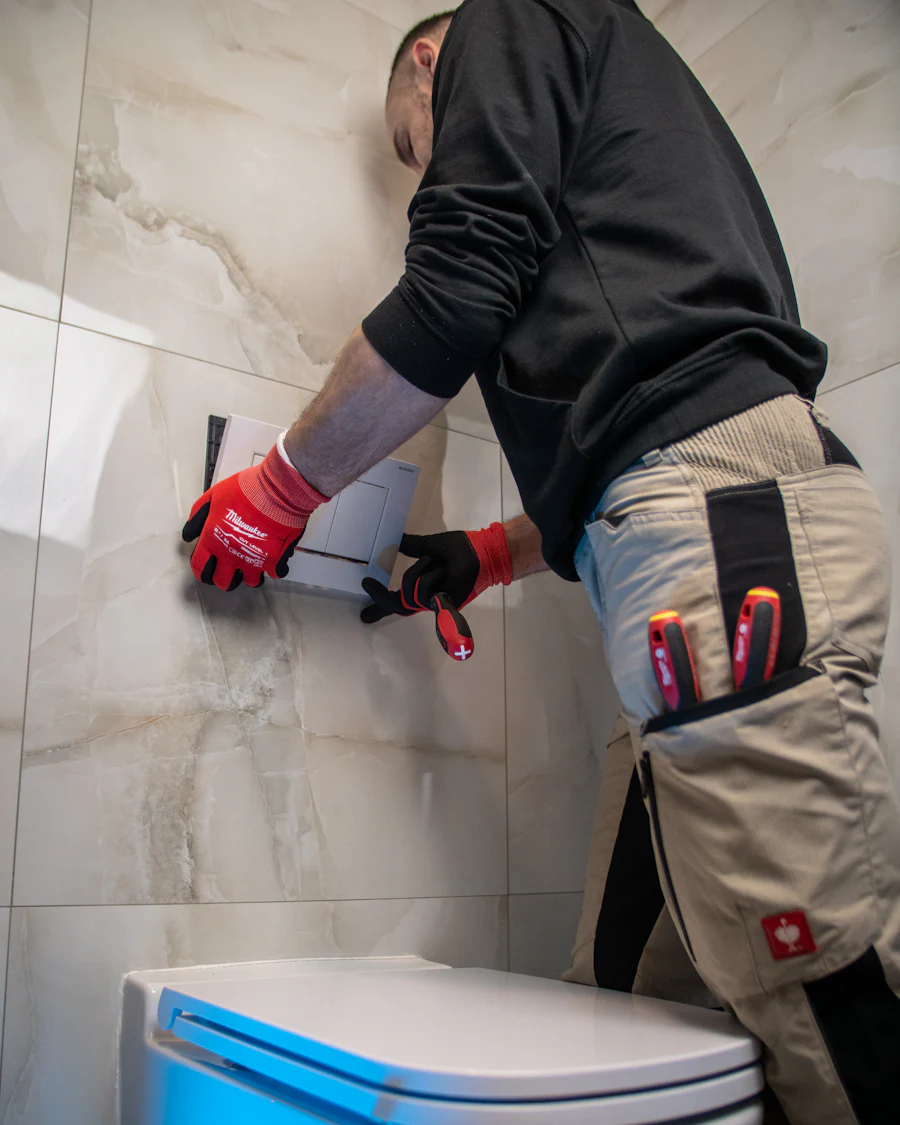 A fitter seen from behind, tiling a bathroom wall above a new toilet