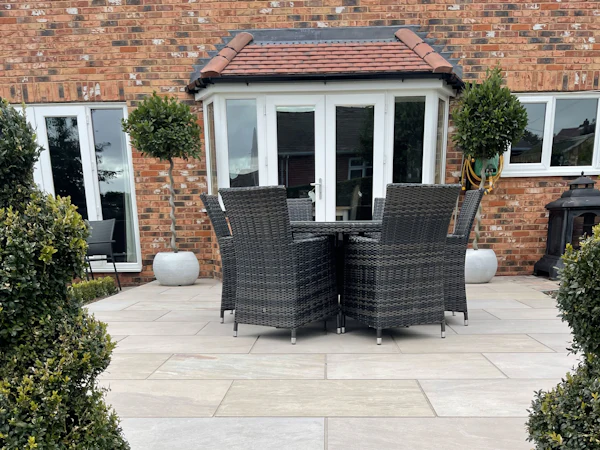 A sandstone patio with a dining table outside the French doors of a brick house