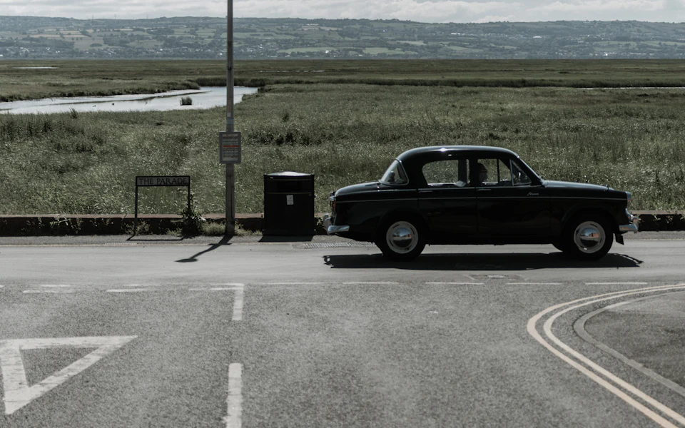 A seafront road beside salt marsh, with hills across the water