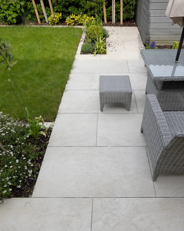 A pale porcelain path beside a lawn, with garden furniture on the patio