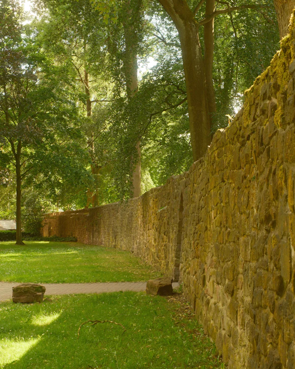 A long warm-coloured sandstone wall beside a lawn under trees