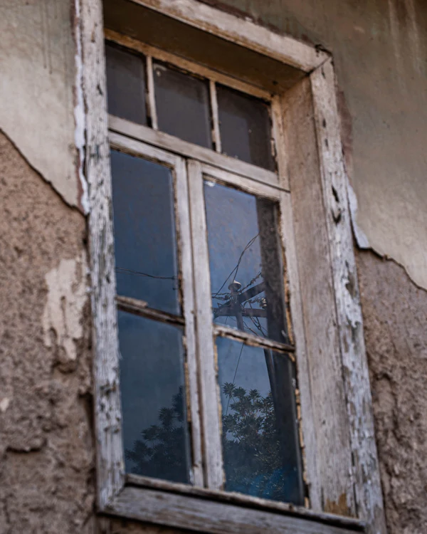 Before: a weathered timber window, the paint gone grey and split, in a crumbling plaster wall