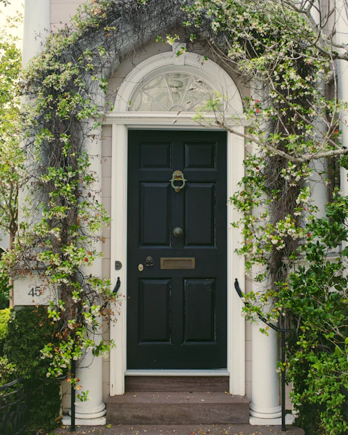 A dark green six-panel front door with a brass knocker under a fanlight, ivy round the doorcase