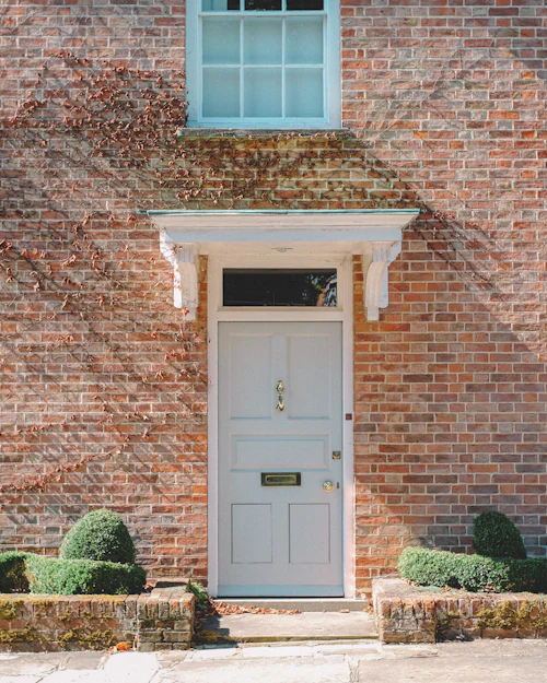 A brick house front with a white panelled door under a small hood and pale blue sash windows either side