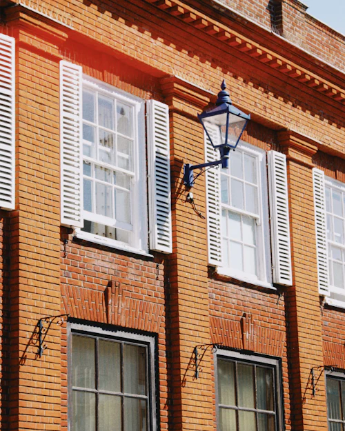 White sash windows with white louvred shutters and an iron lamp on a red-brick Georgian front