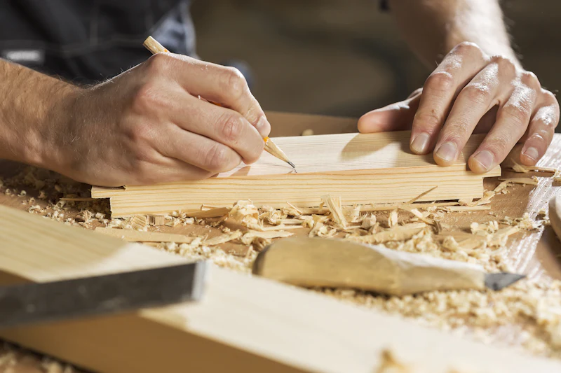 A joiner marking a line on a length of timber with a pencil, shavings on the bench