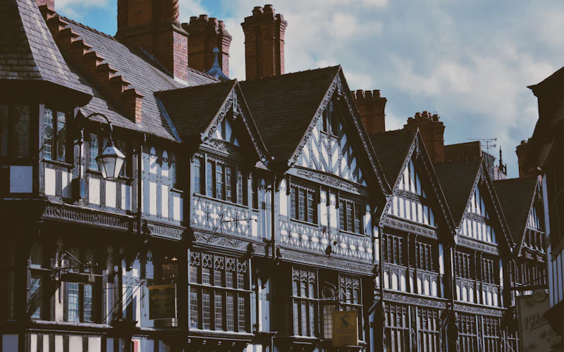 A long run of black-and-white gabled timber frontages with tall chimneys under a blue sky