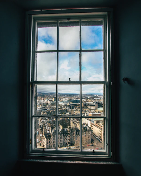 A tall sash window in a deep, dark reveal, looking out over the rooftops of a city