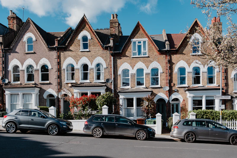 A row of Victorian red-brick villas with bay windows, white sashes and gables, cars parked in front