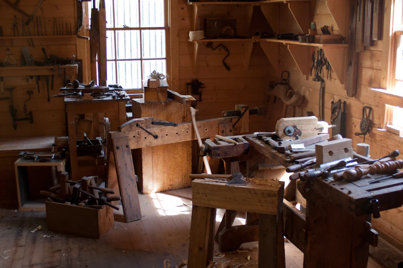 A joinery workshop with heavy wooden benches, vices and tools on the walls, daylight from a window