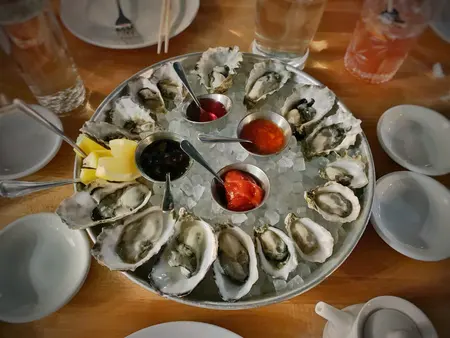Two dozen oysters opened on a tray of crushed ice, with lemon and three small pots of dressing.