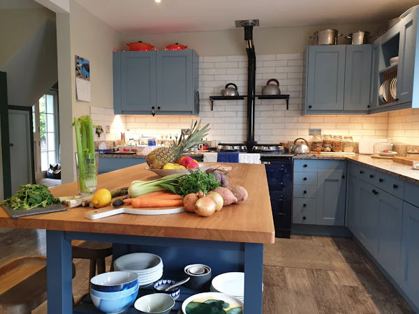A blue-grey painted shaker kitchen with an oak-topped island covered in vegetables