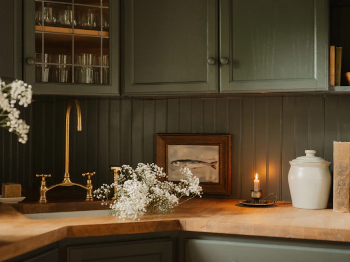 A ceramic sink and brass bridge tap set into an oak worktop, green panelling behind