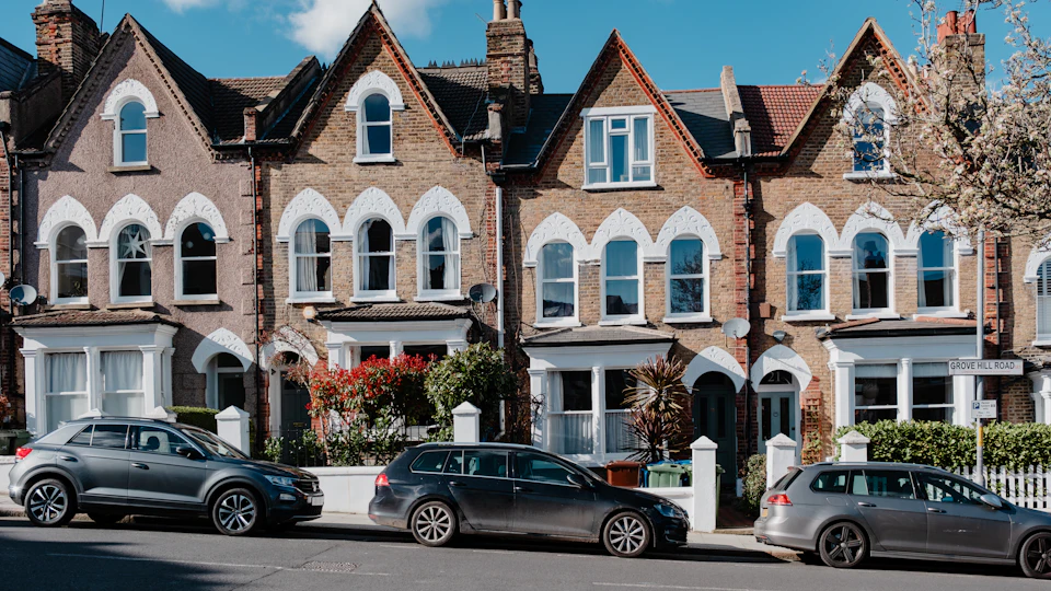 A row of Victorian bay-fronted houses with gables and sash windows, cars parked outside
