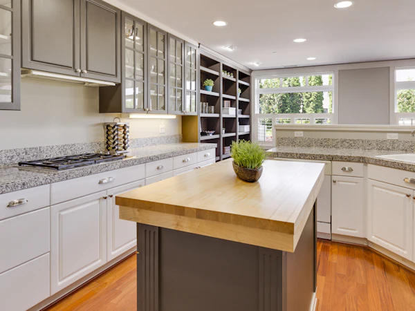 A grey kitchen island with a thick butcher block top among white shaker units
