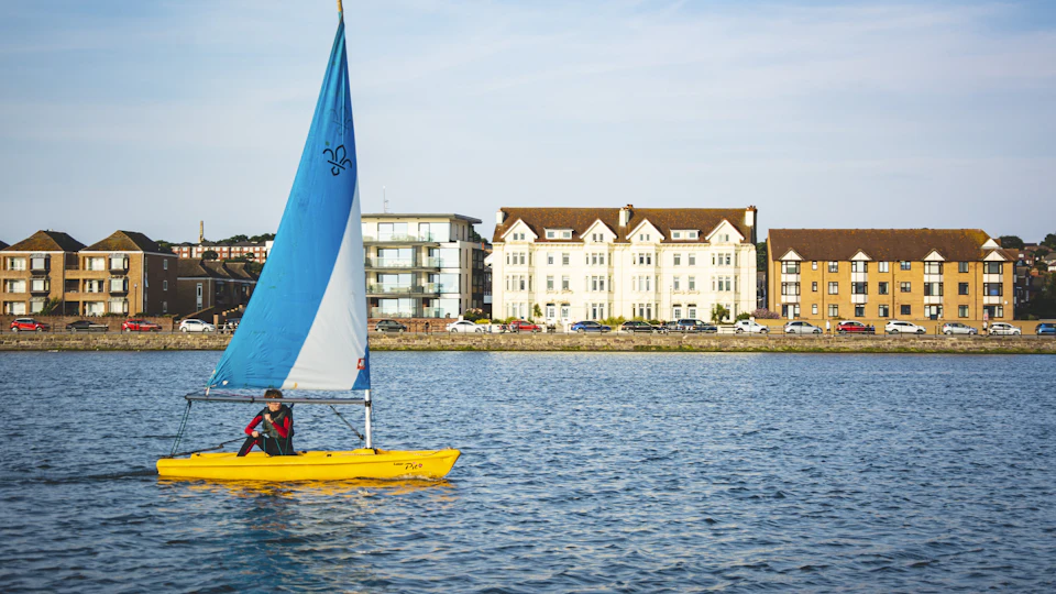 A sailing dinghy on West Kirby's Marine Lake in front of the houses along South Parade