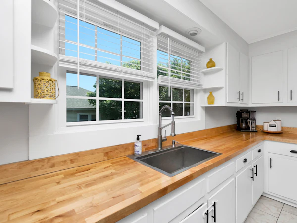 A white shaker kitchen with a long solid oak worktop and an undermount sink under a window