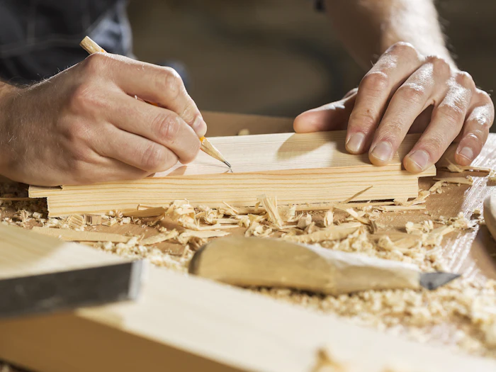 Hands marking a line with a pencil on a length of timber, shavings on the bench