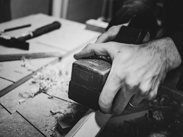 A hand pushing a block plane along a board, in black and white