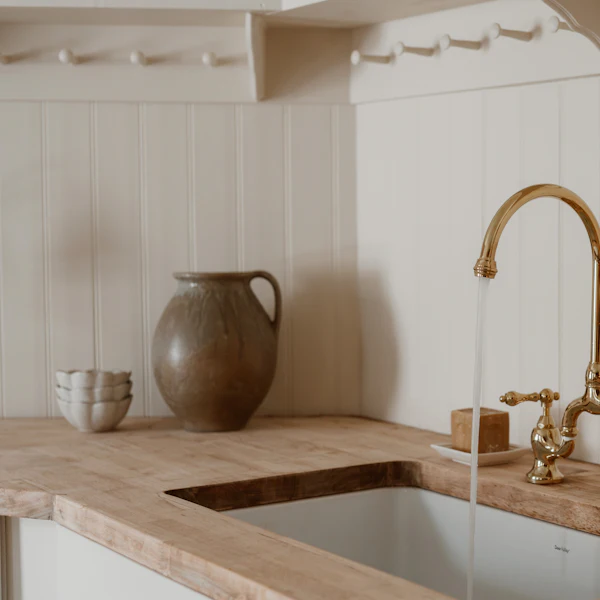 Water running from a brass tap into a white ceramic sink in an oak worktop