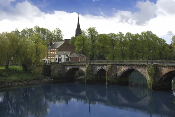 The Old Dee Bridge at Chester under a blue sky, trees and a spire behind