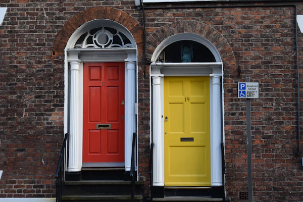 Two Georgian front doors side by side, one red and one yellow, under fanlights in a brick wall