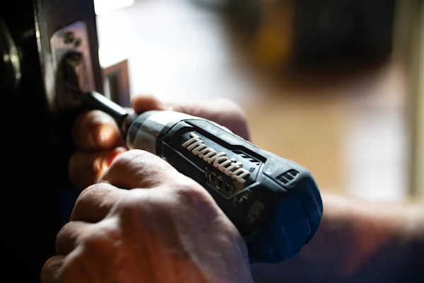 Hands holding a cordless drill against the edge of a door