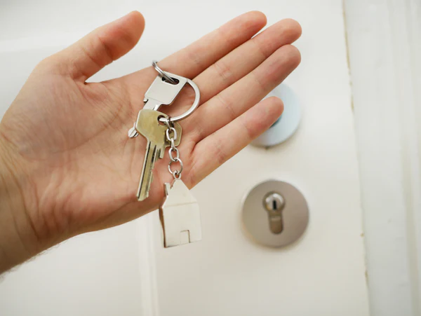 An open hand holding a new set of keys in front of a white door with a euro cylinder lock